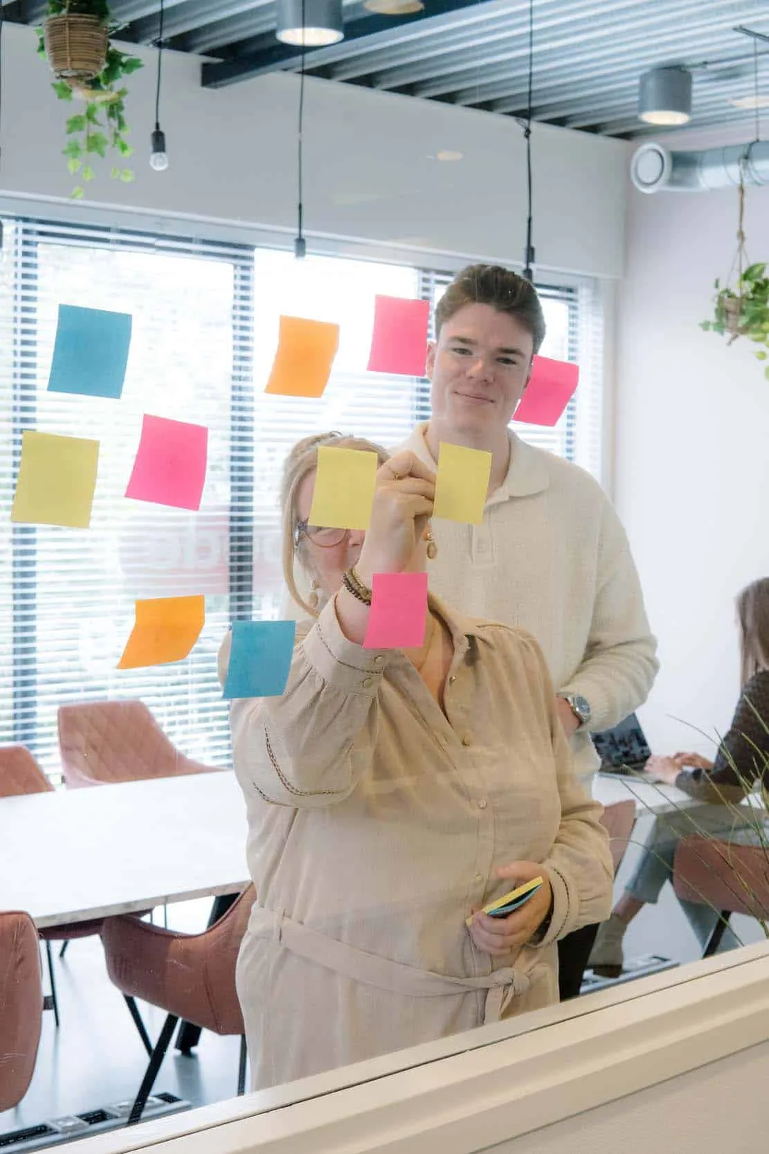 Twee collega’s plakken post-its op de glazen wand