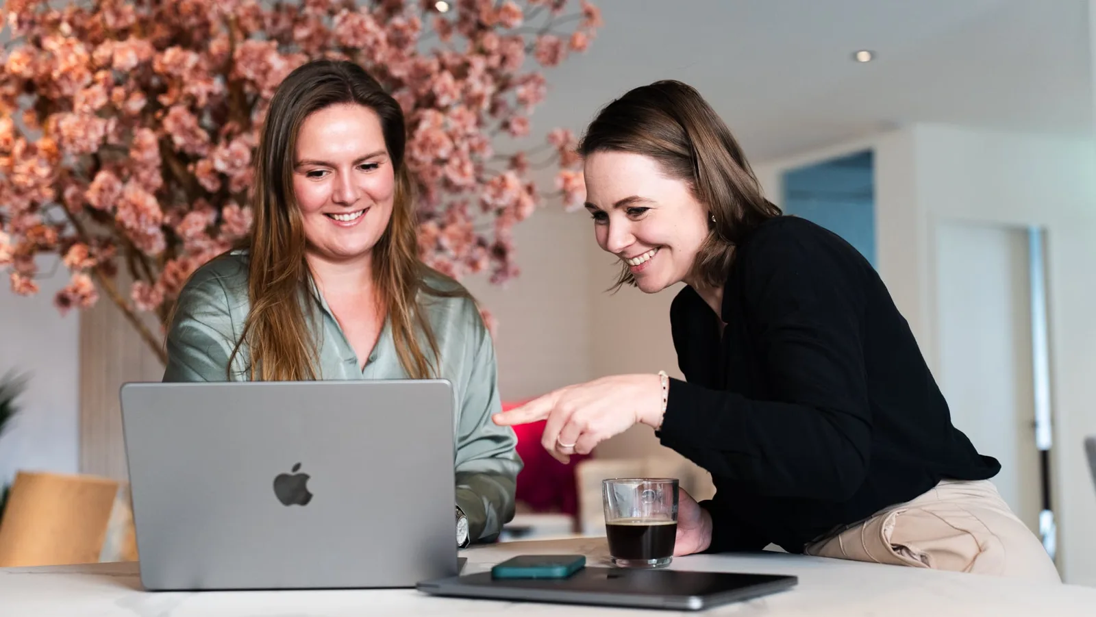 Twee vrouwen werken samen aan een laptop, bespreken de visuele identiteit van een merk. Ze lachen en wijzen naar het scherm, wat een creatieve samenwerking suggereert.